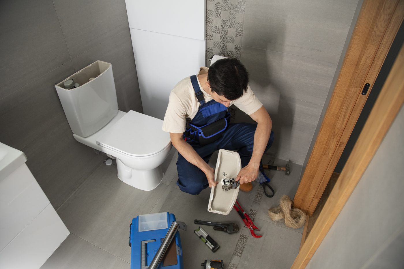 Engineer working on a toilet cistern with tools laid out in a tiled bathroom